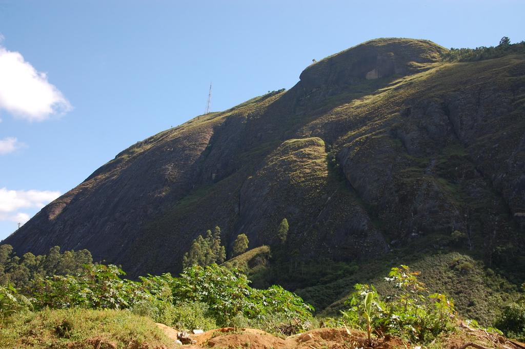 Montanha com vegetação escura e uma torre de rádio em um dia ensolarado.