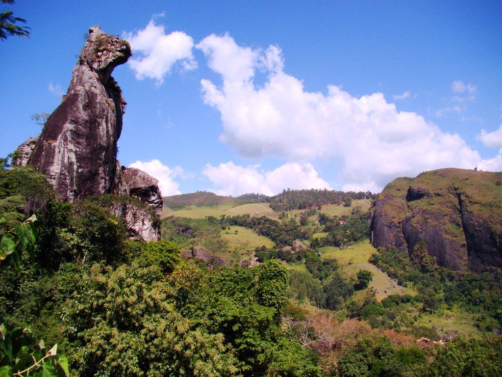 Formação rochosa que lembra a cabeça de um cavalo contra um céu azul brilhante com nuvens dispersas e colinas verdes.
