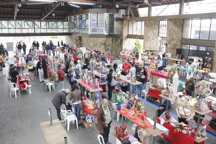 Feira de artesanato em recinto fechado com muitos vendedores e compradores.