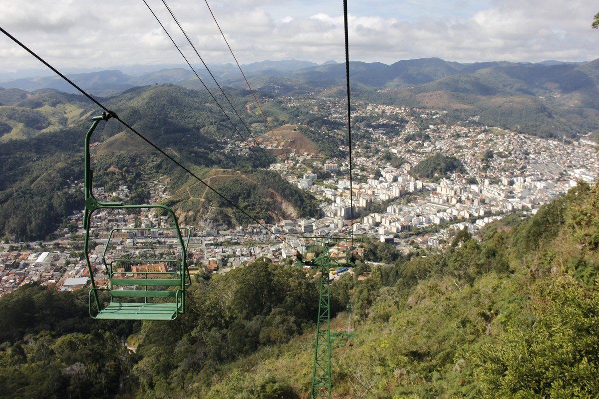 Teleférico verde com vista para uma cidade aninhada entre colinas verdejantes sob um céu límpido.