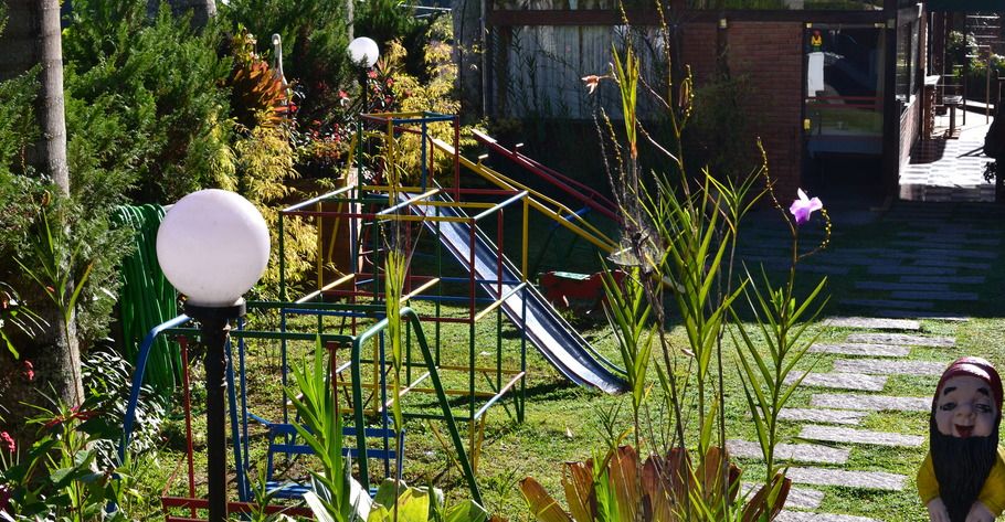 Parque infantil em área gramada com escorregador, rodeado por plantas e um poste de luz.