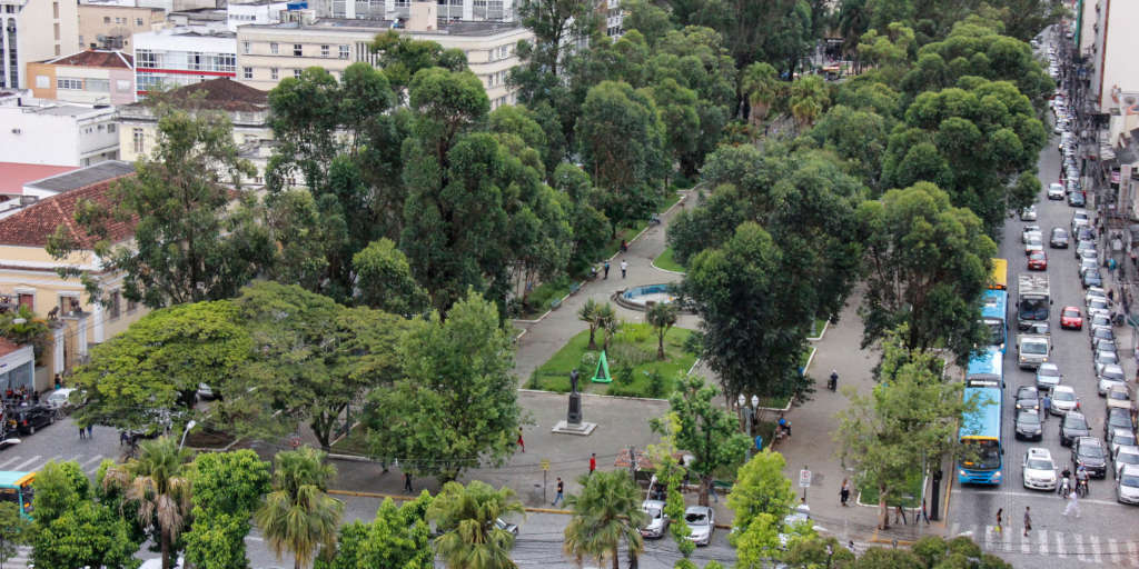 Vista aérea de um parque urbano com árvores, caminhos, edifícios circundantes e trânsito.
