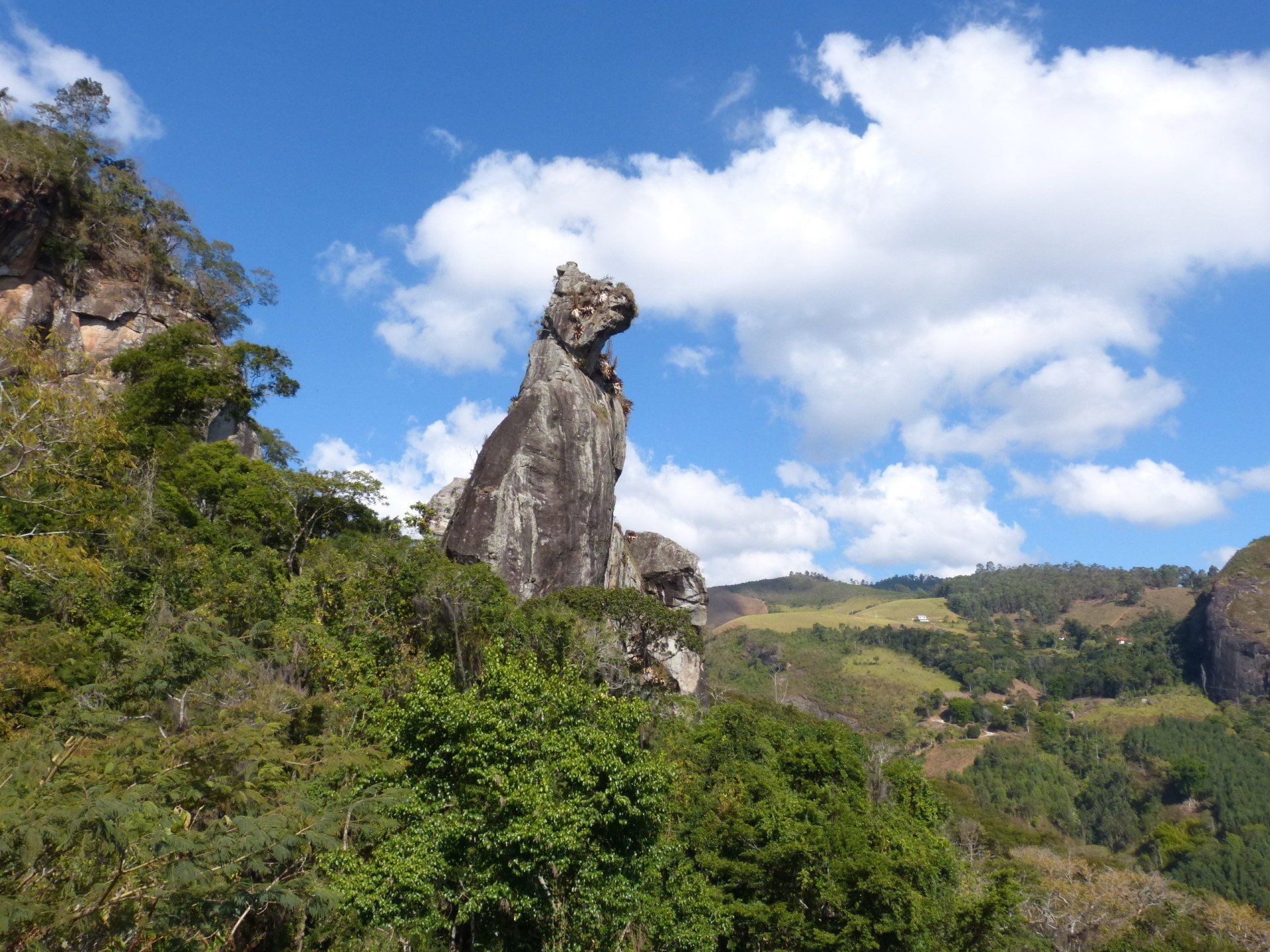 Alta formação rochosa desgastada, que lembra um animal, emoldurada por um céu azul com nuvens brancas.