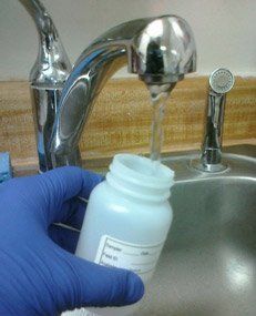 A person wearing blue gloves is pouring water into a sink