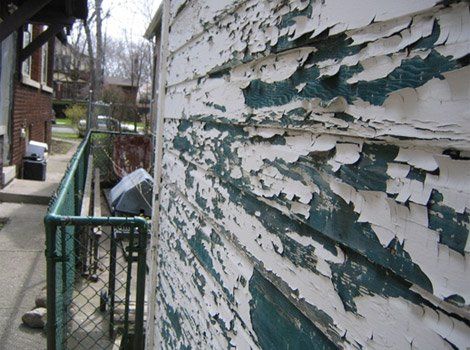 The side of a building with peeling paint and a chain link fence