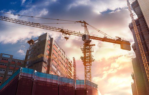 A construction site with cranes and buildings under construction at sunset.