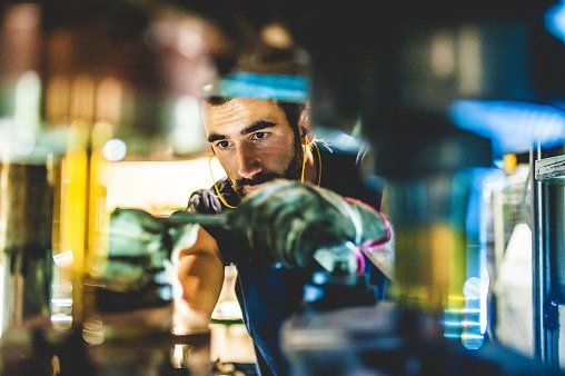 A man with a beard is working on a machine in a factory.