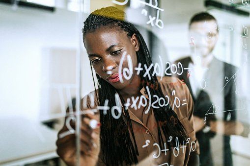 A woman is writing on a glass board with a marker.