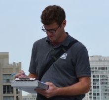 A man wearing glasses is holding a clipboard and writing on it.