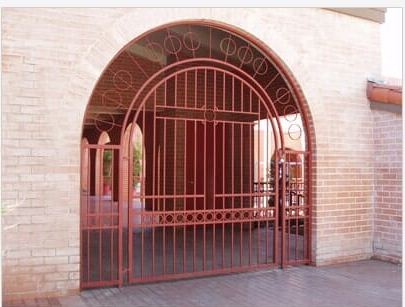 Red iron gate under an arched brick entryway.