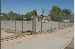 Chain link fence surrounding a paved area with an open gate; daytime.