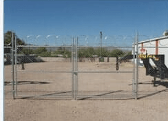 Metal gates with barbed wire topping, in a dirt lot.