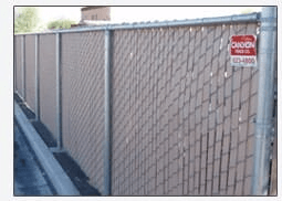Chain-link fence with tan privacy slats. A sign on the fence has the name 
