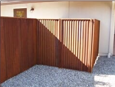 Brown wooden fence enclosing a gravel area, casting a shadow from sunlight.