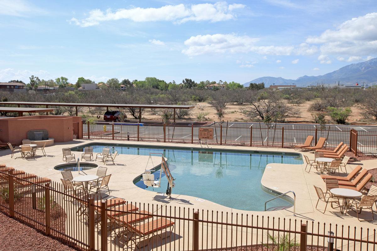 Pool area with lounge chairs, tables, and a mountain backdrop under a blue sky.