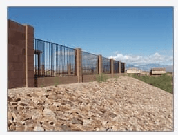 Brown fence with metal bars on a rocky hill under a blue sky.