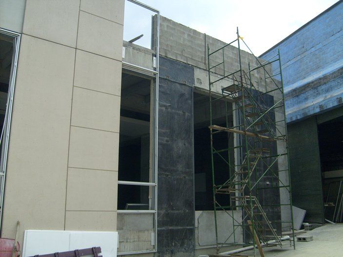 Edificio en construcción; paredes exteriores con paneles beige y láminas negras, andamios presentes.