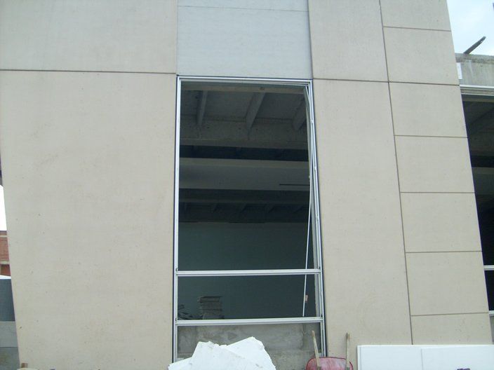 Exterior del edificio con una ventana abierta, marco de metal gris y paneles de color marrón claro.