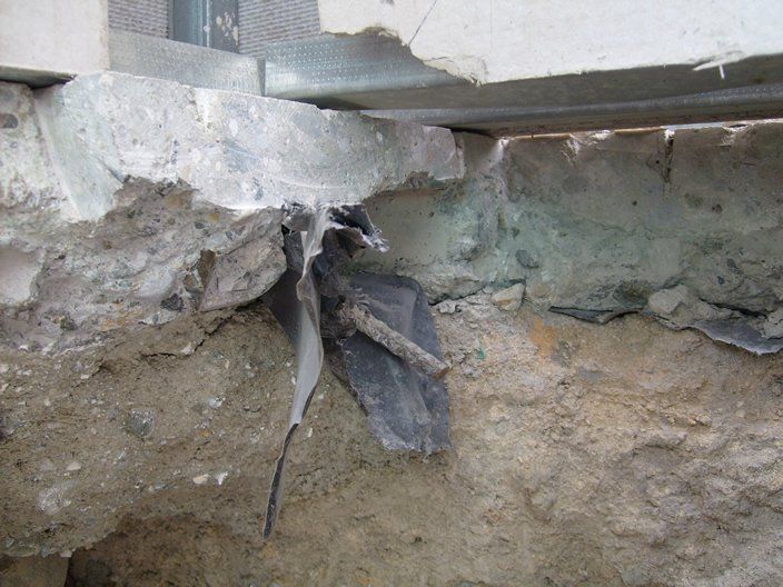Daños en cimientos de hormigón con barras de refuerzo expuestas y material negro.