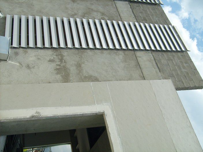 Exterior de edificio con muros de hormigón y lamas metálicas horizontales.