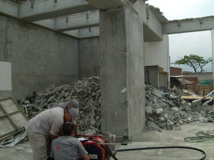 Obreros demoliendo una estructura de hormigón; se ven un montón de escombros, herramientas y vigas expuestas.