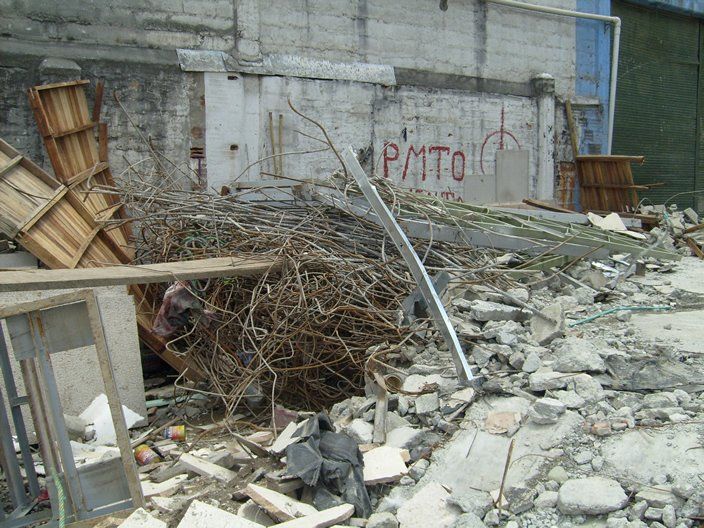 Montón de escombros de hormigón, madera, metal y ramas frente a un edificio con grafitis.