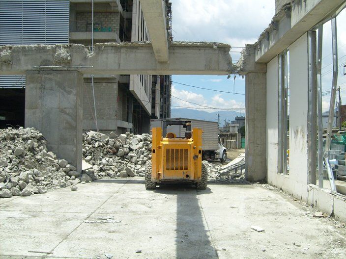 Vehículo de construcción amarillo limpiando escombros debajo de vigas de hormigón.