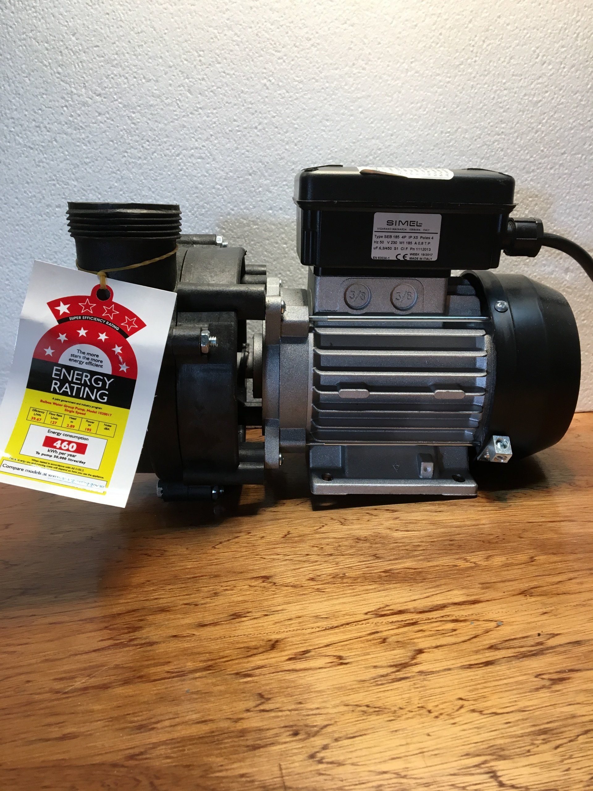 Small silver and black electric motor or pump on a wooden surface with a hanging tag.