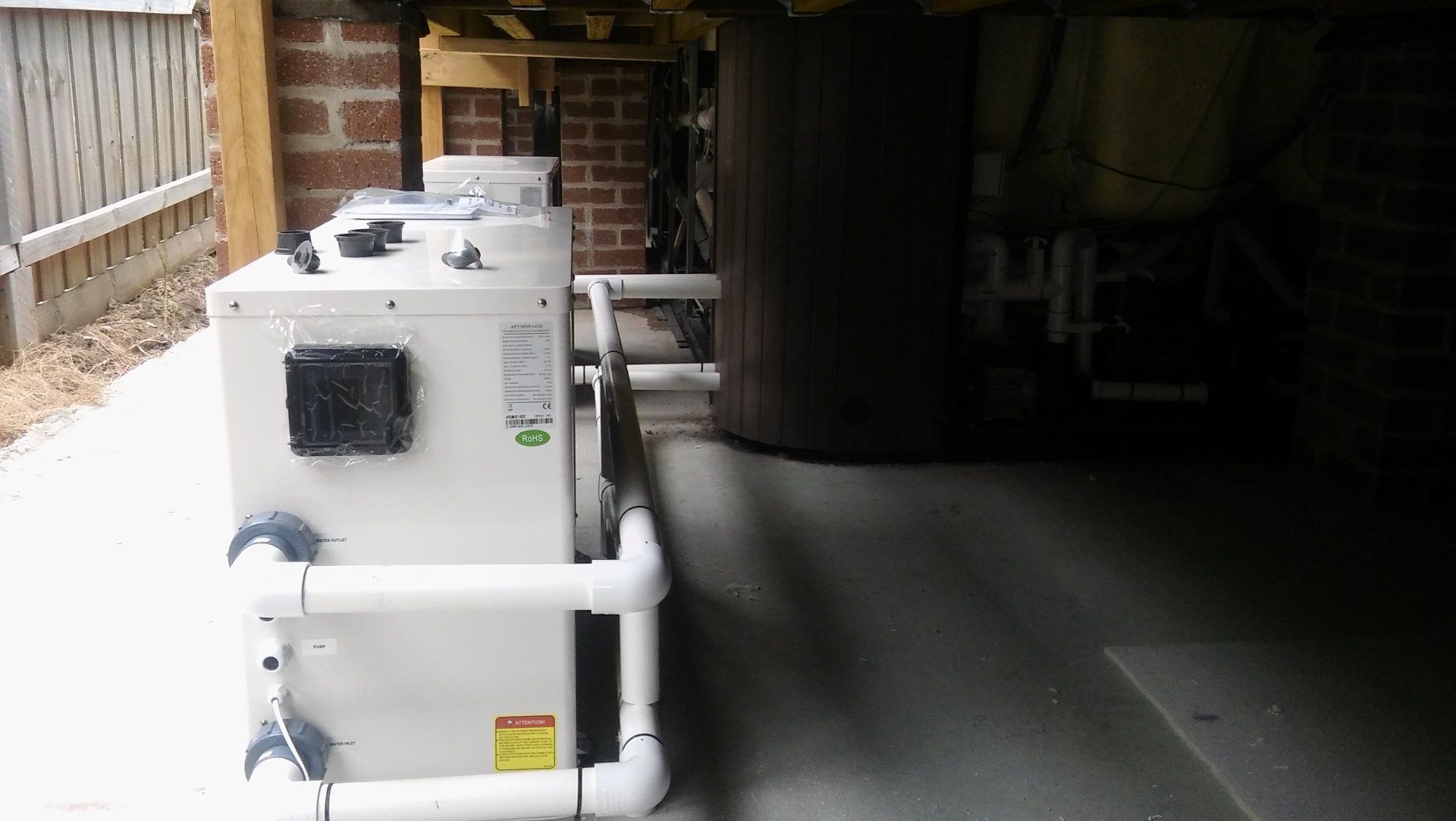 White HVAC unit with pipes beside a wooden fence in a dark industrial area