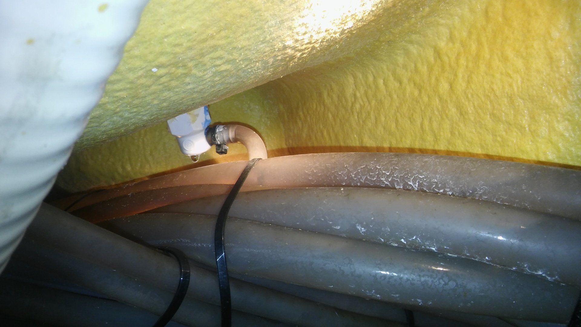 Close-up of a white electrical connector and black cable against a yellow and gray insulated surface.