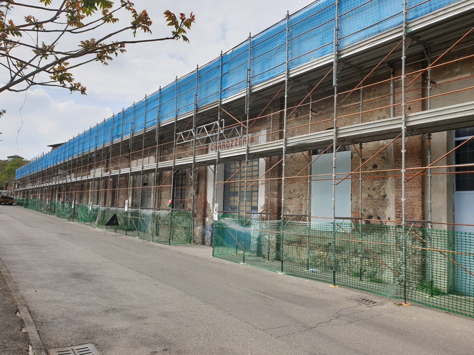 Edificio in fase di ristrutturazione con impalcature e reti di sicurezza blu lungo una strada.