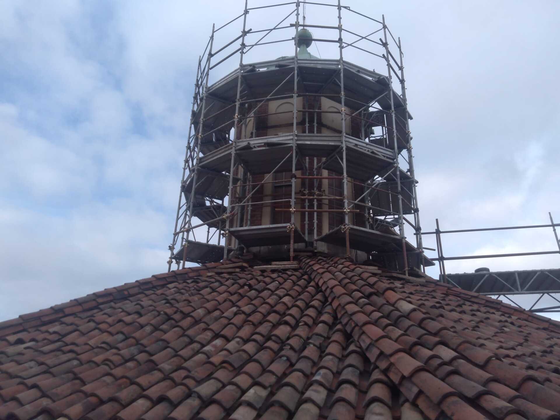 Un'impalcatura circonda la struttura a cupola di un edificio con un tetto di tegole in terracotta sotto un cielo nuvoloso.