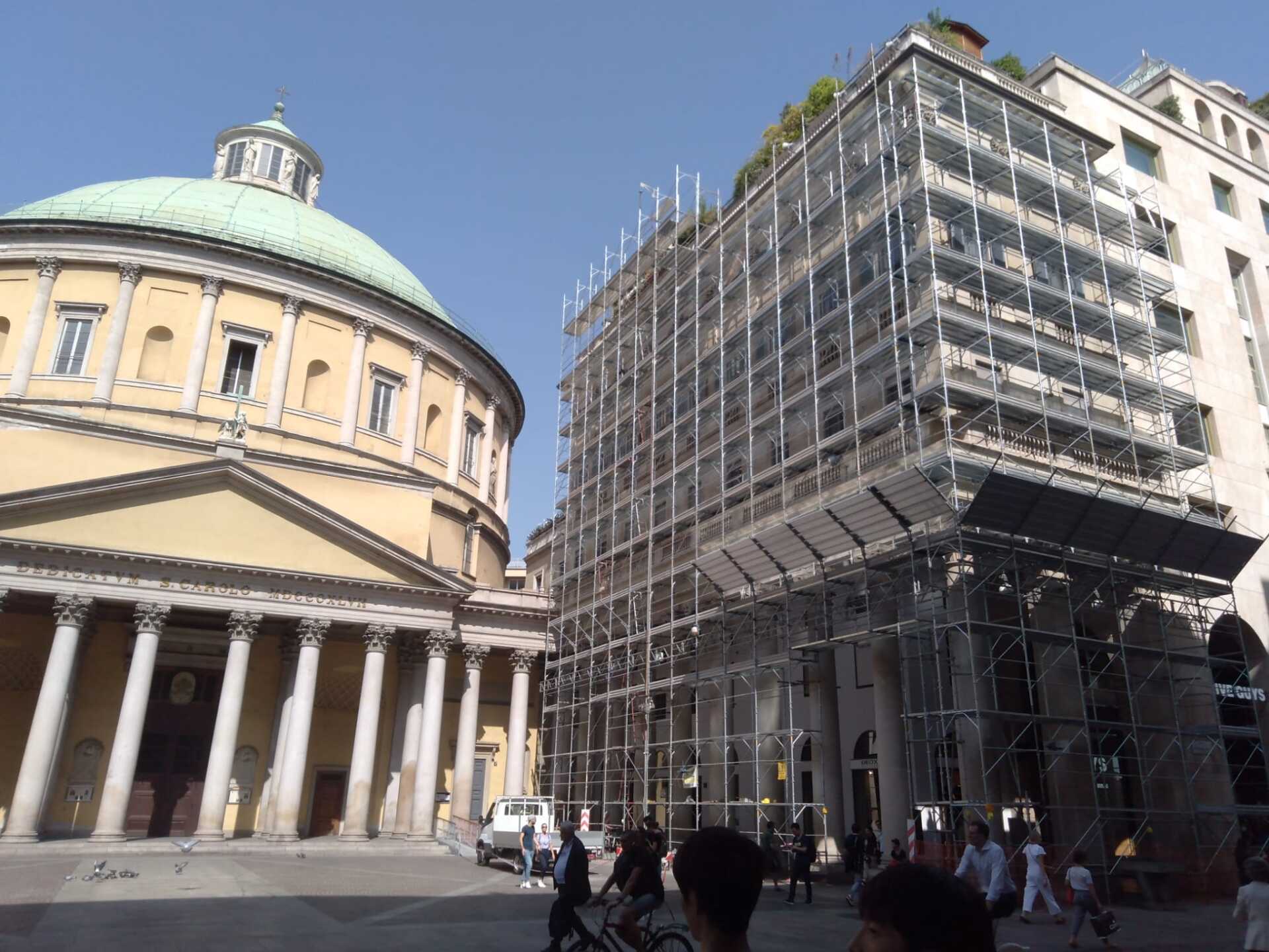 Edificio con cupola e colonne, impalcature sull'edificio adiacente, persone nella piazza.