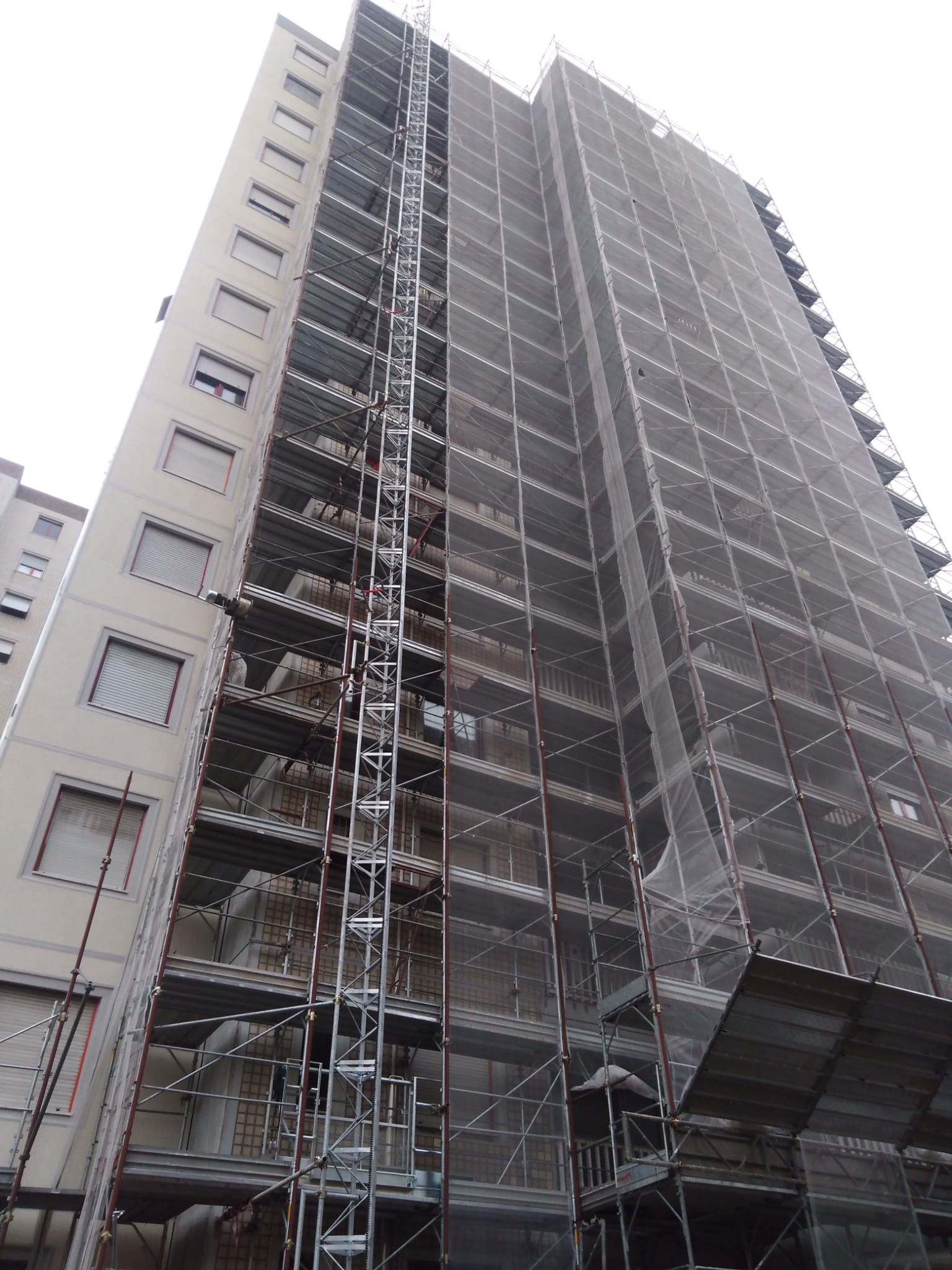 Edificio alto in costruzione, coperto da impalcature e reti di sicurezza.