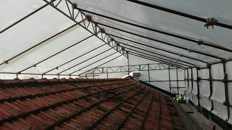 Vista di un tetto di tegole coperto da una pensilina trasparente realizzata con travi metalliche e tessuto bianco.