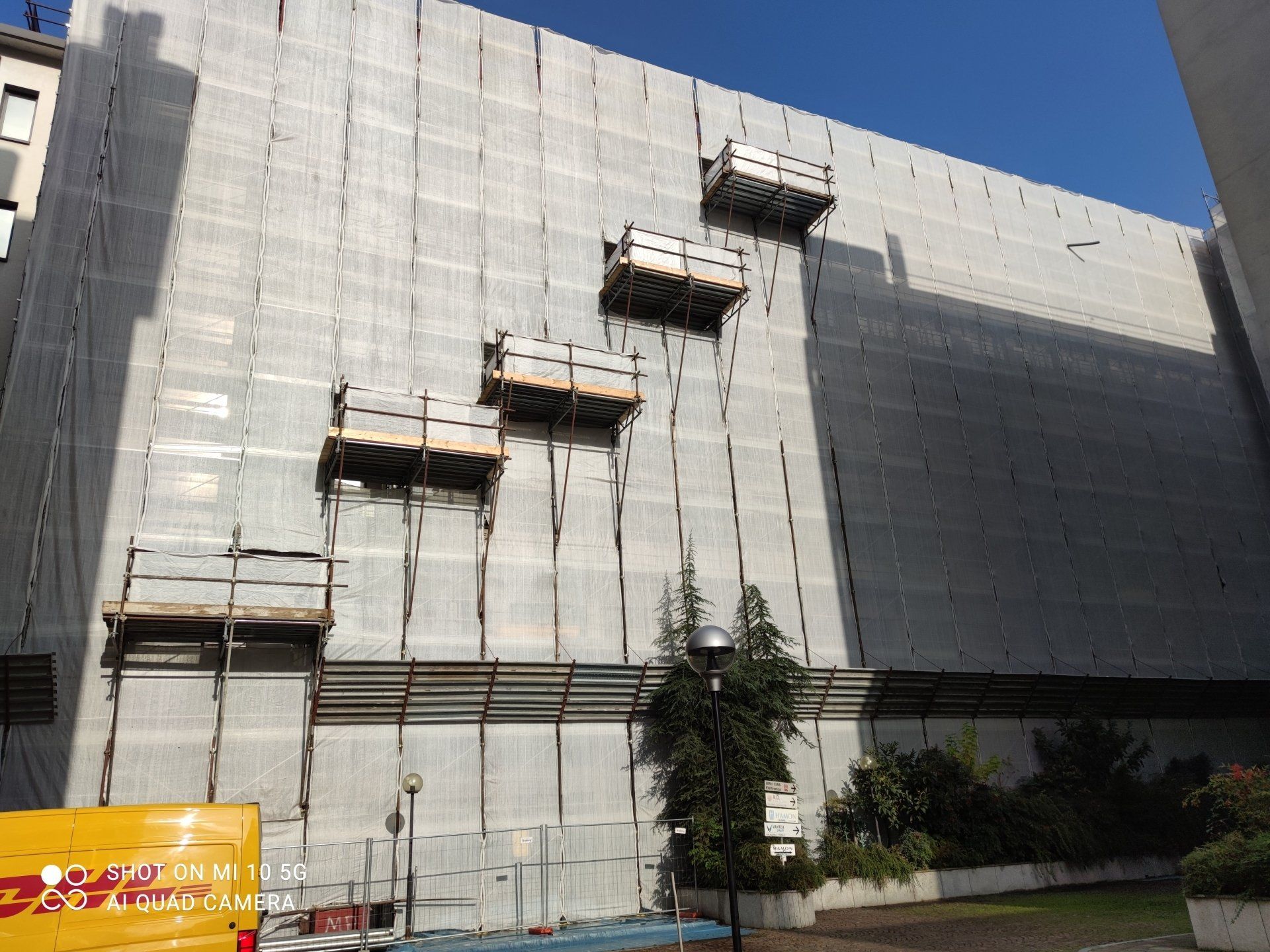 Facciata dell'edificio ricoperta di impalcature e reti, con diverse piattaforme di lavoro collegate.