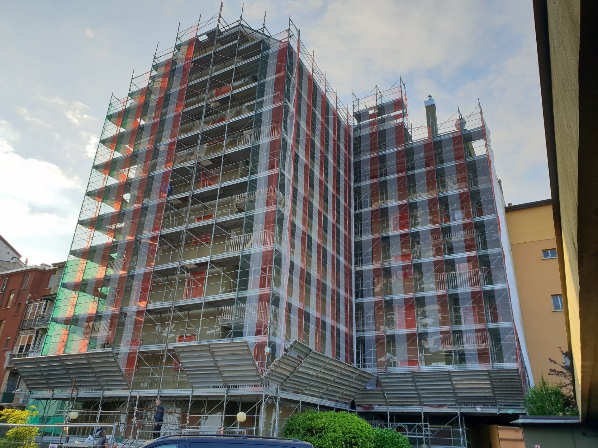 Edificio in fase di ristrutturazione, coperto da impalcature e reti di sicurezza, con un cielo nuvoloso sullo sfondo.