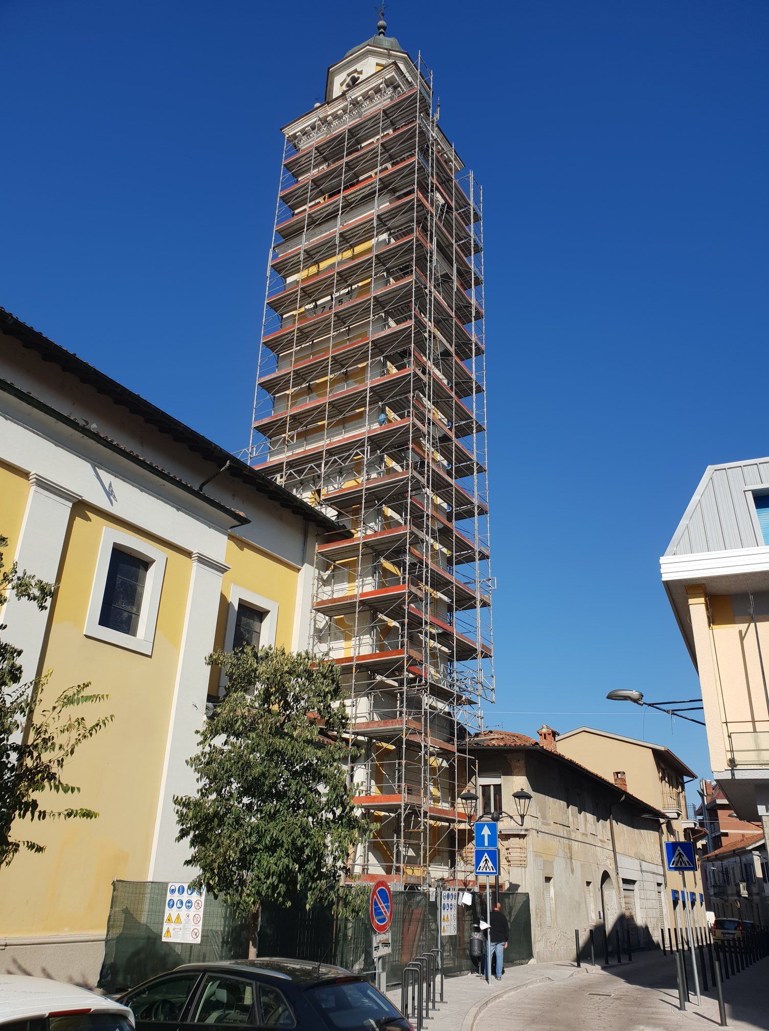 Un'alta torre sotto un'impalcatura in una giornata di sole in Italia. Edifici e strada in primo piano.
