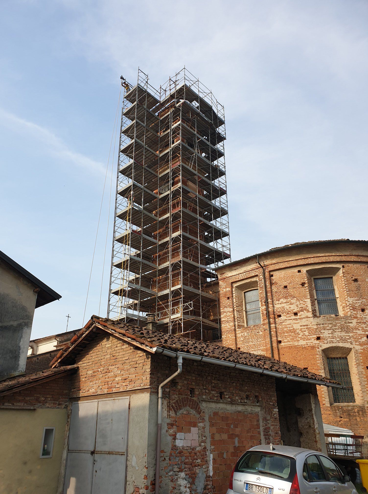 Un alto edificio in mattoni in costruzione, avvolto da impalcature. Un'auto è parcheggiata davanti ad altri edifici.