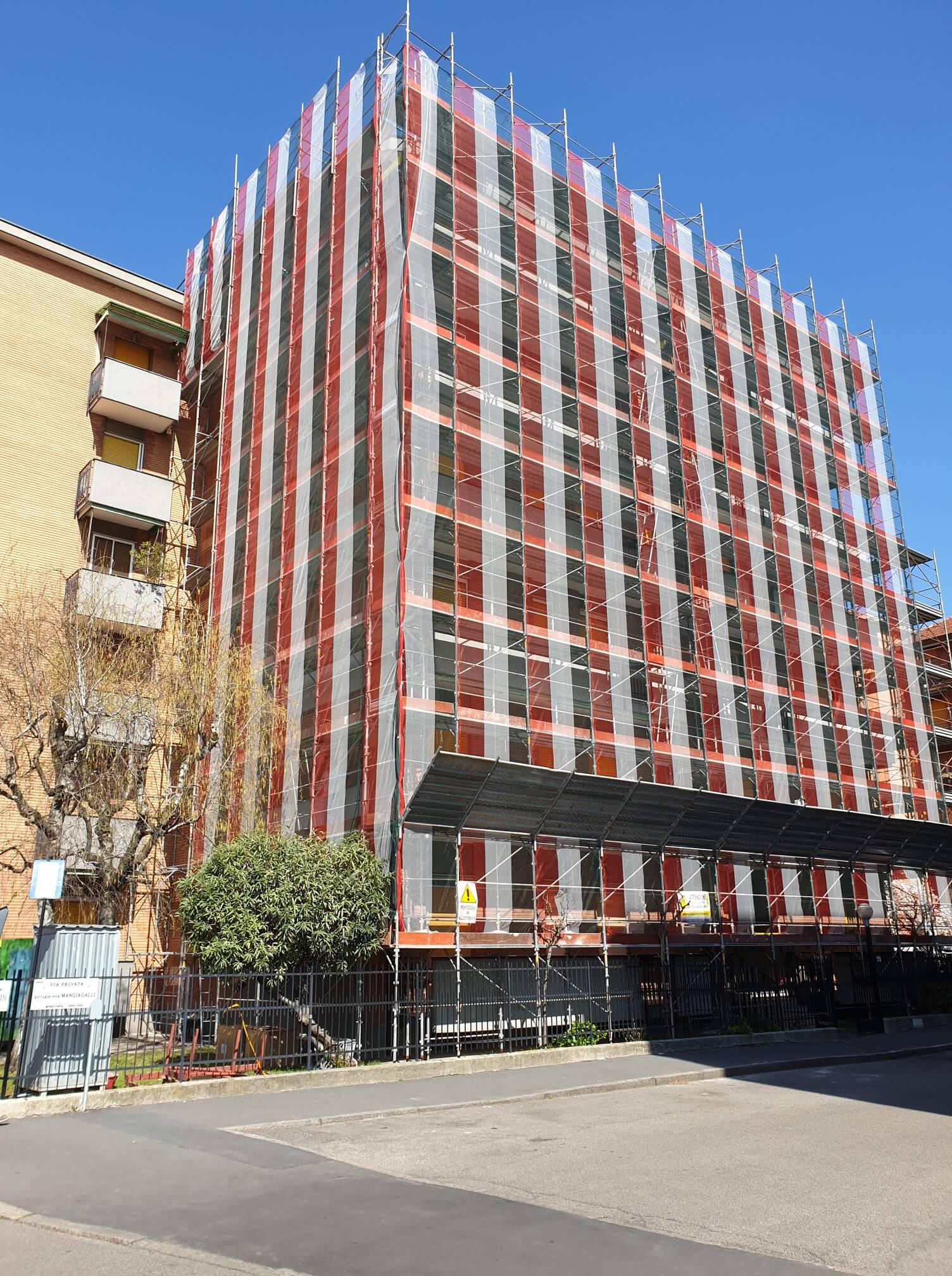 Edificio in fase di ristrutturazione, ricoperto da impalcature a strisce rosse e grigie.