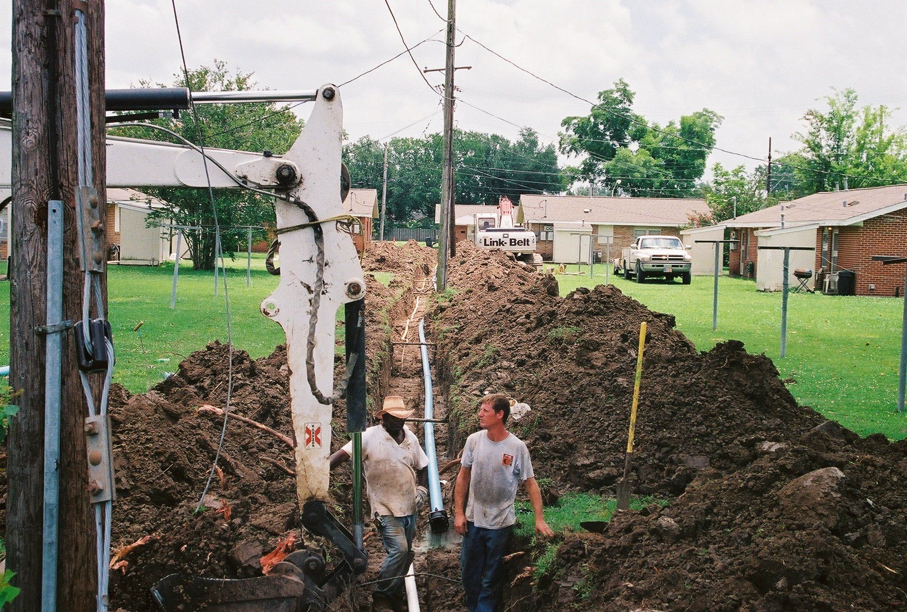Two men are standing in a pile of dirt near a telephone pole
