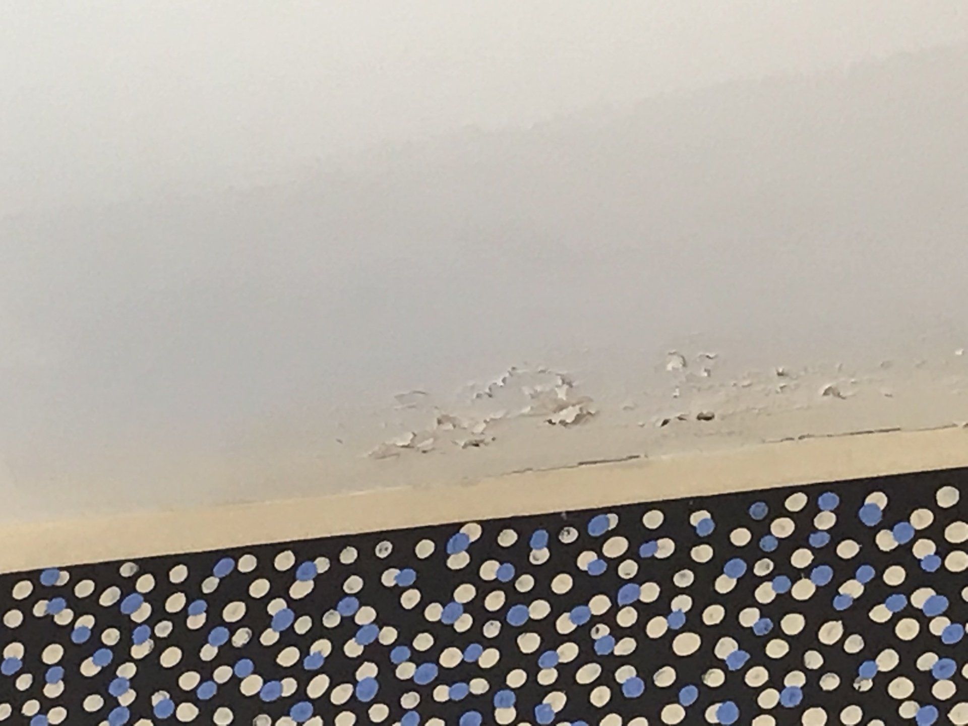 Ceiling with peeling paint near exterior wall caused by moisture leaking into the home via the masonry wall