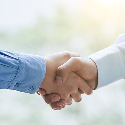 Two people are shaking hands in front of a window.