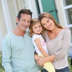 A man and woman holding a little girl in front of a house