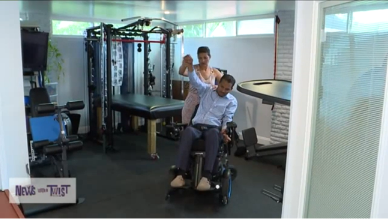 A man in a wheelchair is being helped by a woman in a gym.
