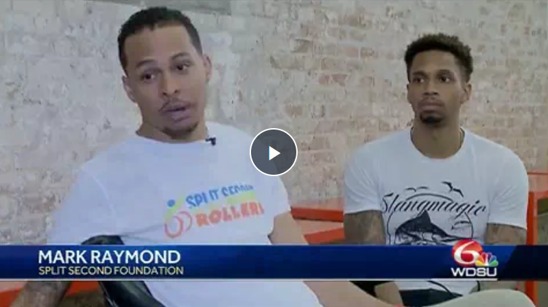 Two men are sitting next to each other in front of a brick wall.