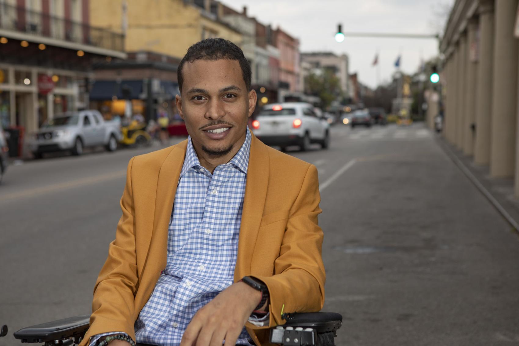 A man in a yellow jacket is sitting in a wheelchair on a city street.