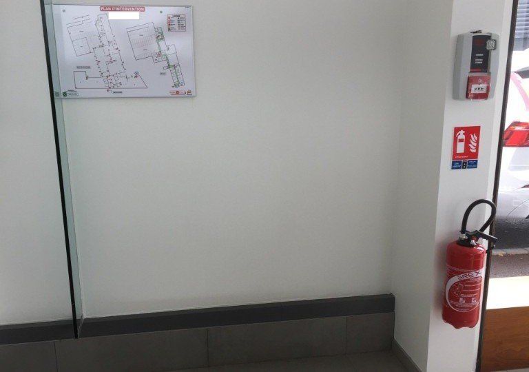 Un extincteur rouge est accroché sur un mur à côté d'un tableau blanc.