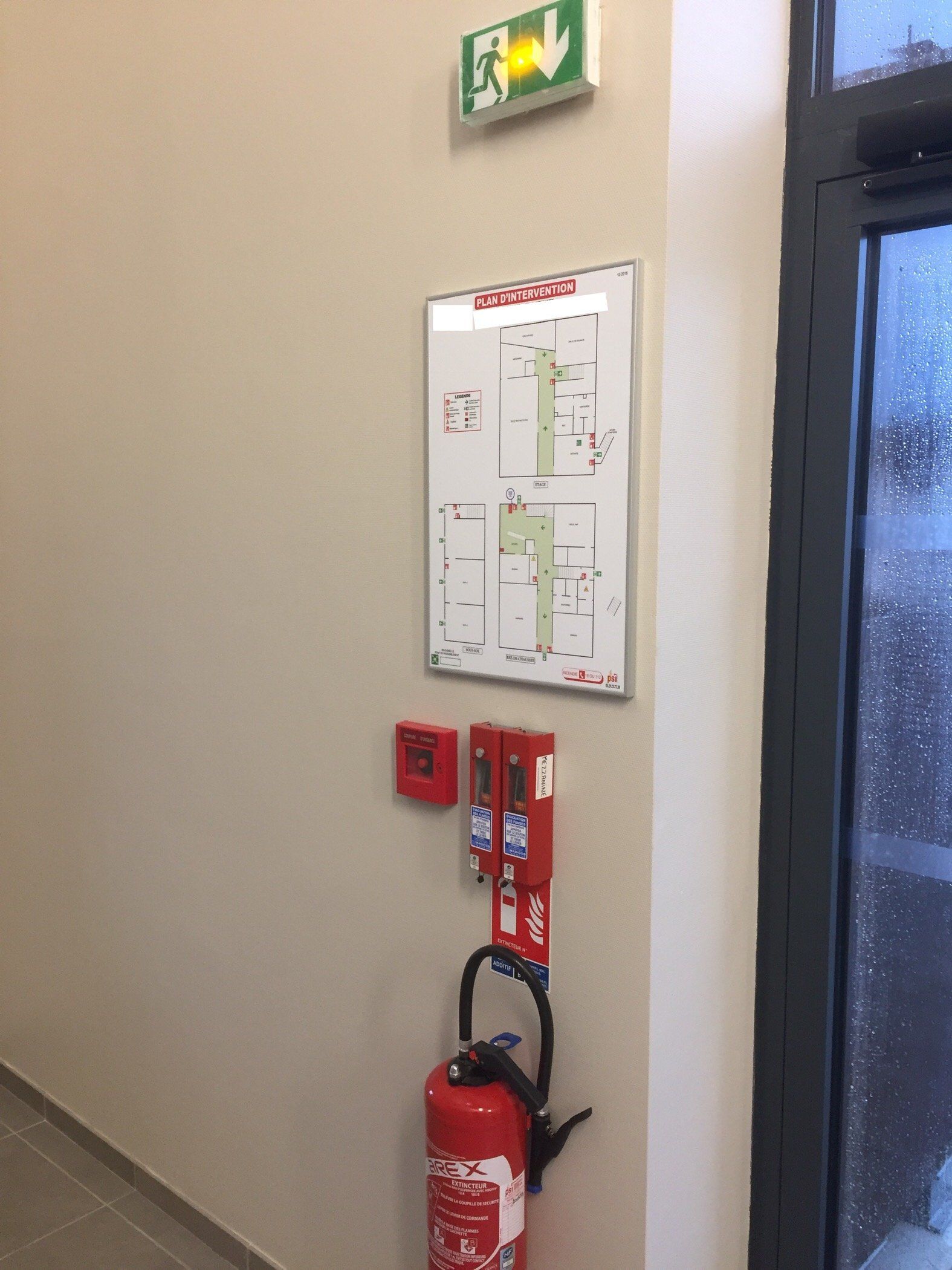 Un extincteur est placé dans un couloir à côté d'un panneau de sortie de secours.