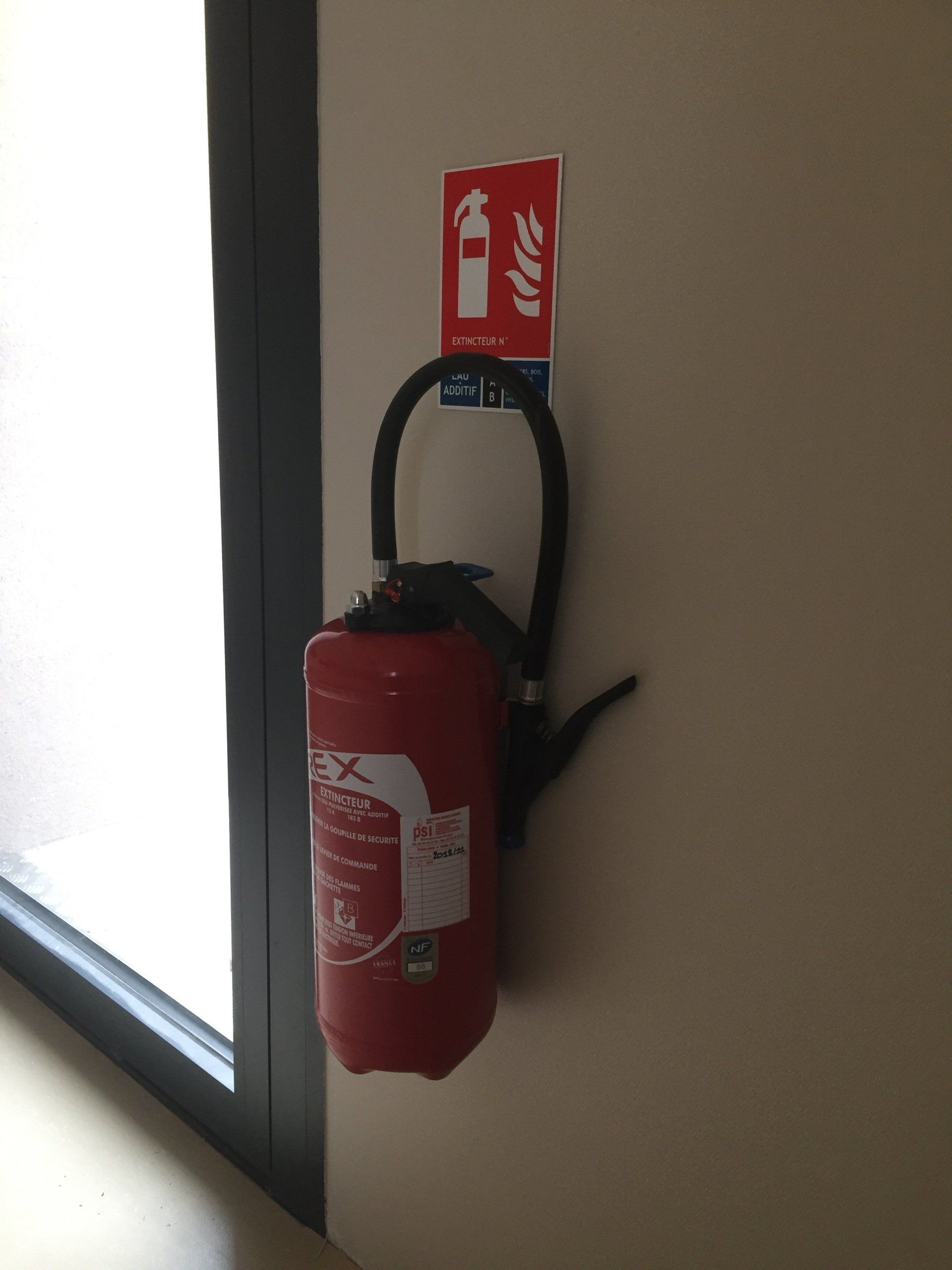 Un extincteur rouge est accroché sur un mur à côté d'un panneau indiquant le feu